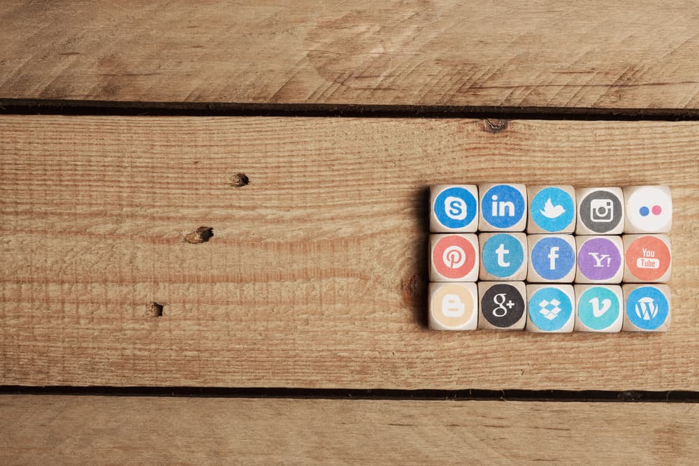 Mesa de madeira com vários quadradinhos de madeira, cada um com o logo de uma rede social (twitter, linkedin, instagram, youtube, skype, etc)